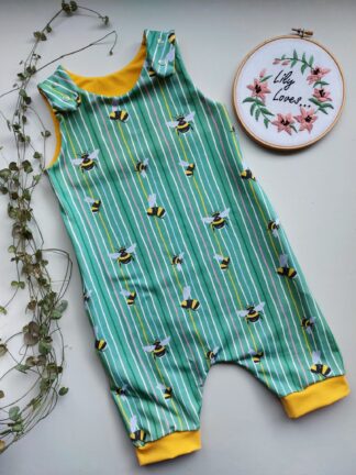 A Grow With Me summer romper with short legs, in a stripey fabric with bees and yellow cuffs.