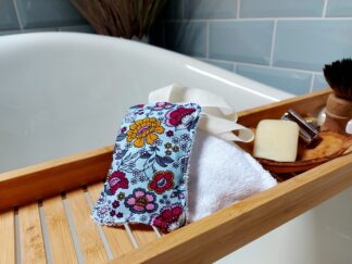 Two shower scrubs sit on a bath tray, one shows a retro floral print and the other baboo towelling on the reverse