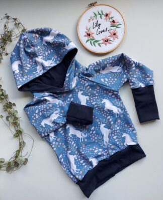 A childrens hoodie in unicorn print with navy cuffs, waistband and hood lining. THe cuff of one sleeve is rolled up to show the Grow With Me feature.
